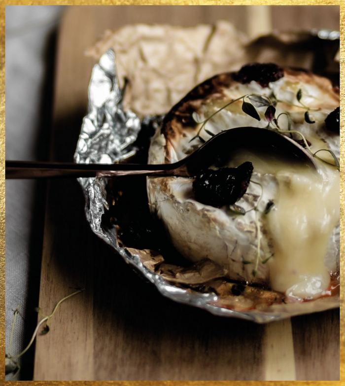 A baked wheel of brie, topped with herbs & broken with a spoon so cheese oozes out.