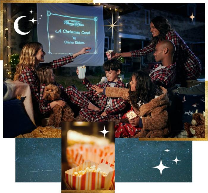 An extended family in matching red & navy check PJ sets watching a movie outdoors on a projector, with blankets & popcorn.