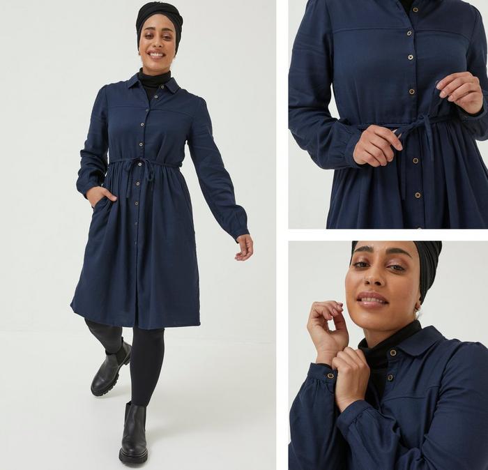 Woman modelling a long-sleeved shirt dress in cloth material and navy blue colour, with tie waists.