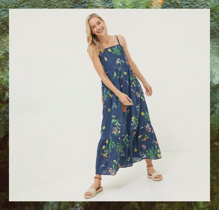 A blonde woman modelling a shift dress; navy blue base with floral and wild flower printing.