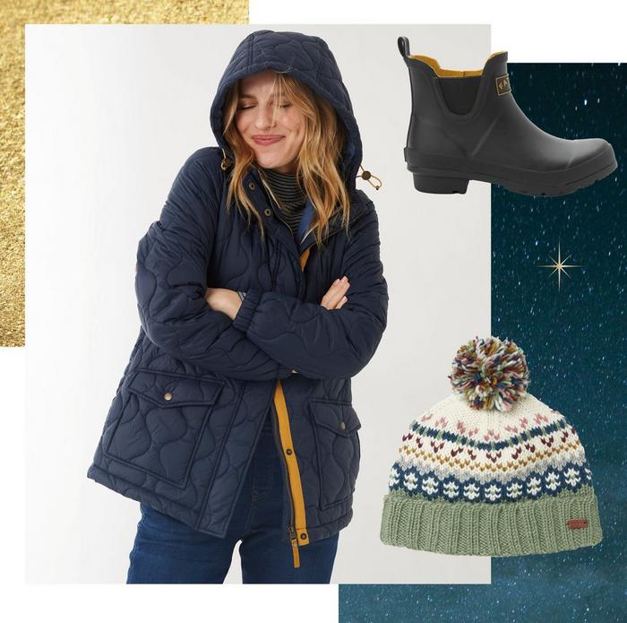 A woman wearing a navy puffer jacket. A black ankle-height welly. A knitted bobble hat with Fair Isle pattern.