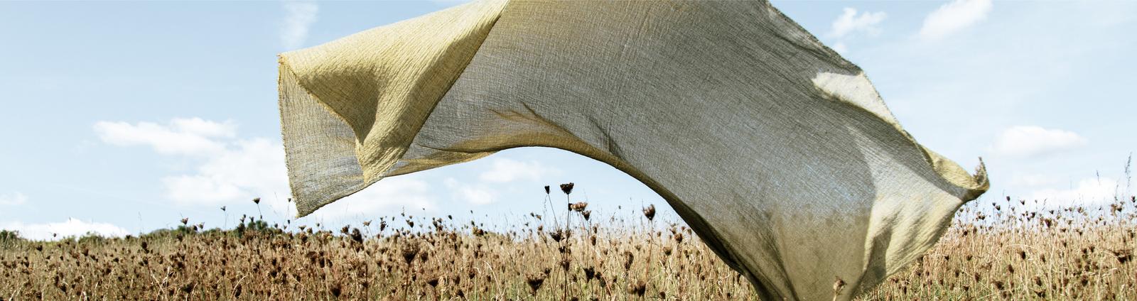 A piece of khaki green linen fabric floating over a meadow beneath a blue sky.