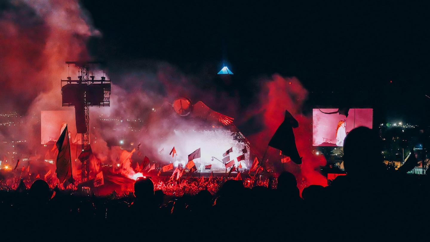 Dramatic red lighting illuminates a massive audience at Glastonbury festival.