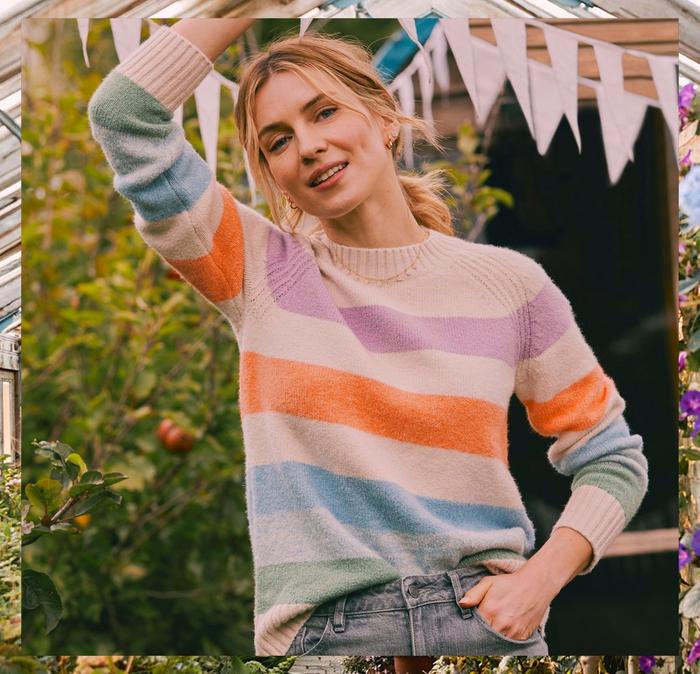 A woman wearing a high-neck jumper with pastel-coloured block stripes, & grey jeans.
