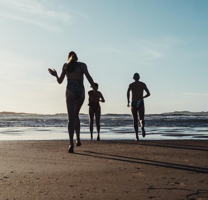 A group of people in summer swimwear running into the sea.