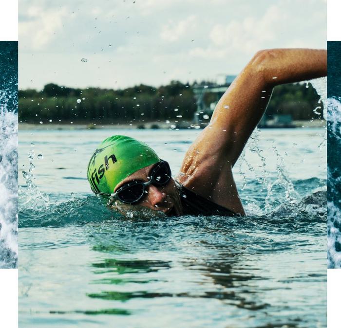 A man wearing a bright green swimming cap & black goggles, swimming front crawl in open waters.