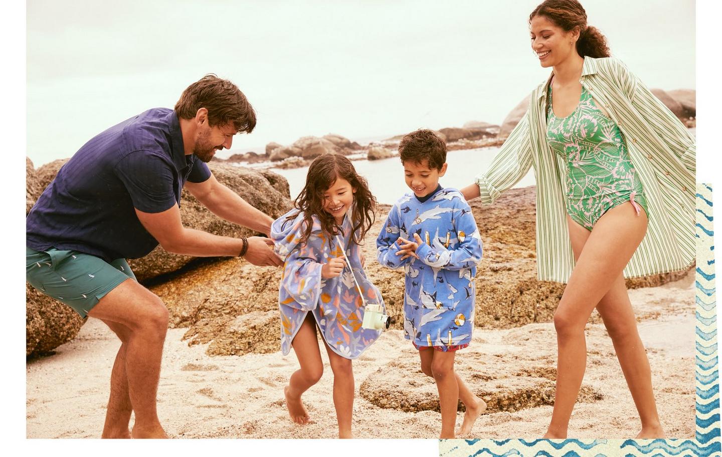 A family on the beach; the adults dressed in summer shirts & swimwear, the kids with towel ponchos over swimwear.
