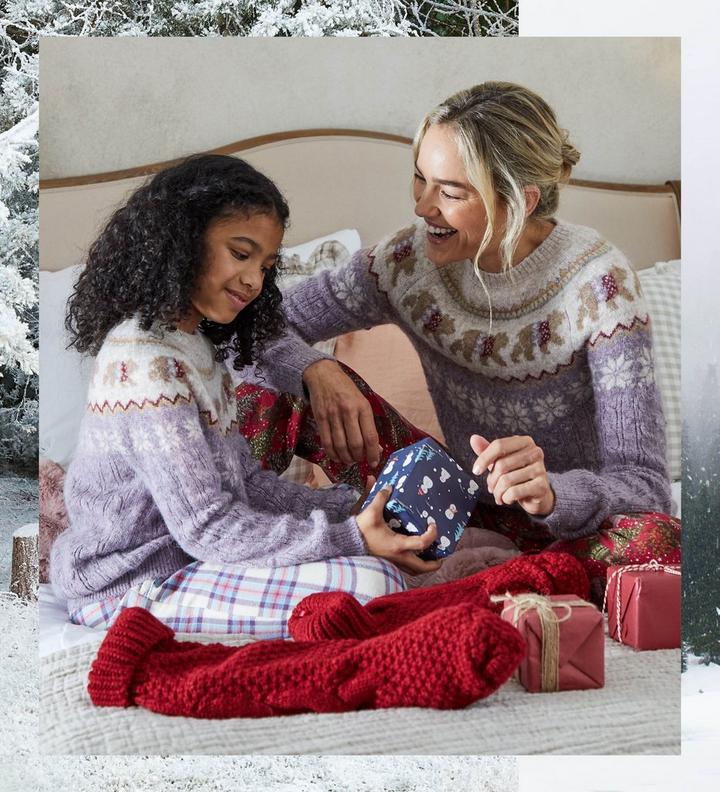 A girl and a woman in matching polar bear patterned Christmas sweaters, opening presents together.