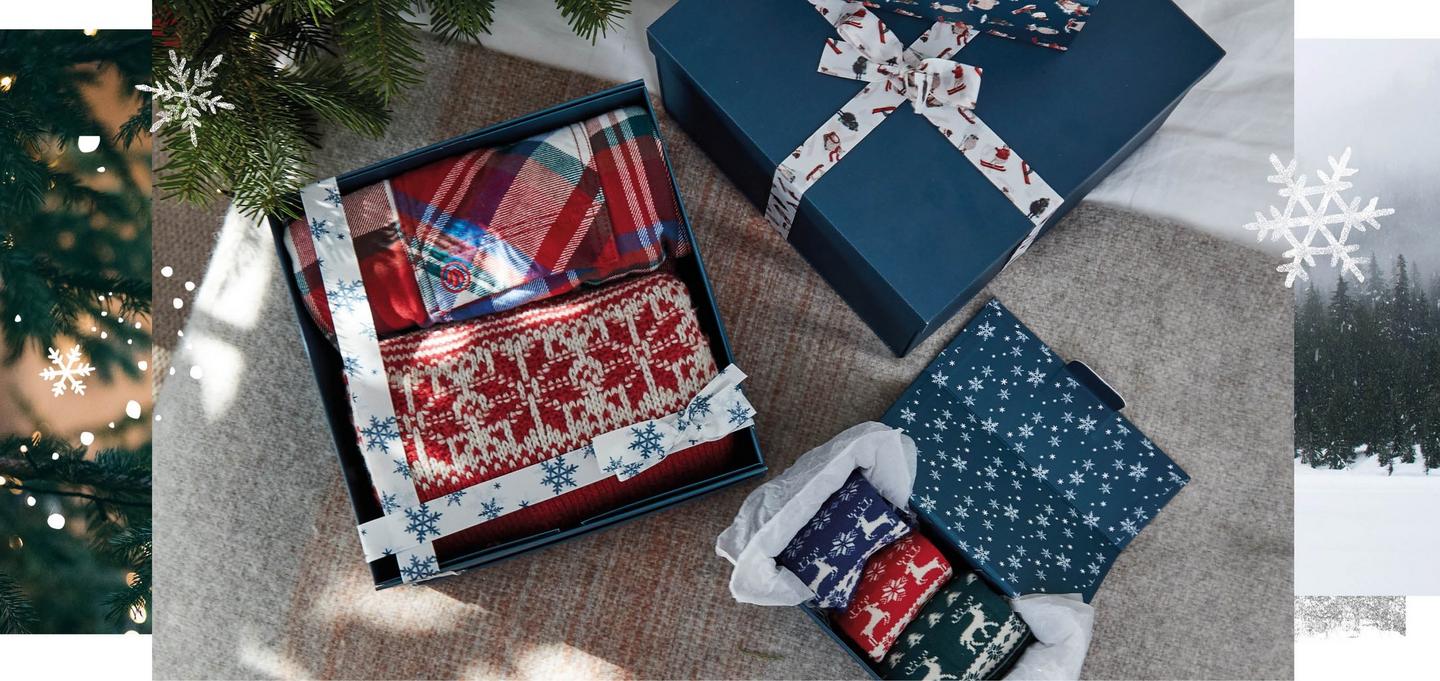 Blue gift boxes of knitwear, nightwear and socks, decorated with fabric ribbons, beneath a Christmas tree.