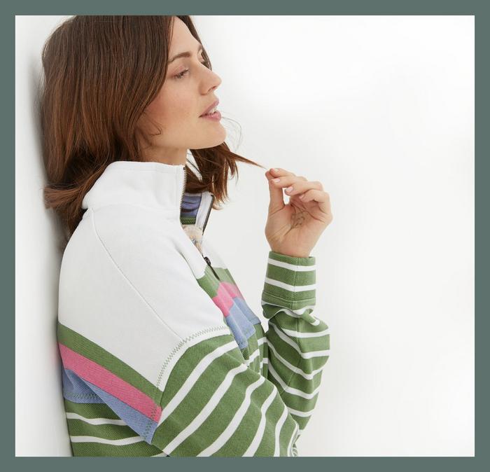 A woman wearing a pique cotton sweatshirt with white, pink, blue & striped-green panels, & a zip half-neck.