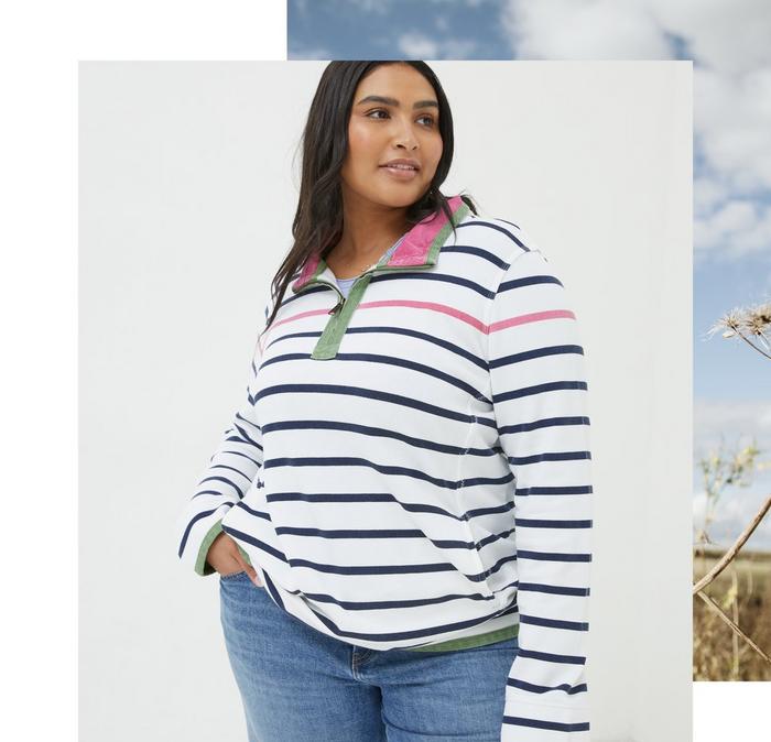A woman wearing a white & navy Breton-style striped Airlie sweatshirt with green contrast zip neck & pink collar lining.