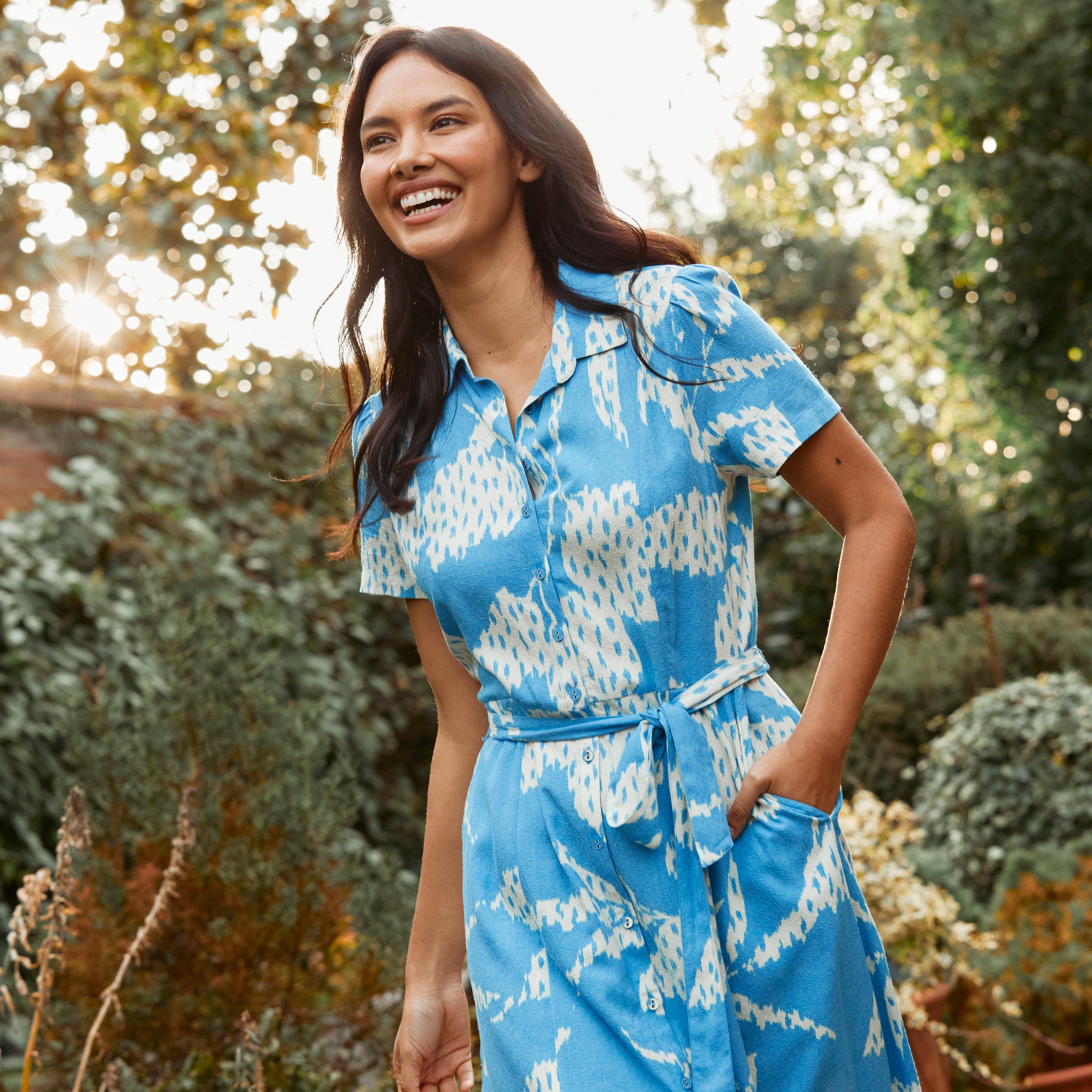 A woman wearing a bright blue shirt dress with textured leaves print, short sleeves & tie waist.