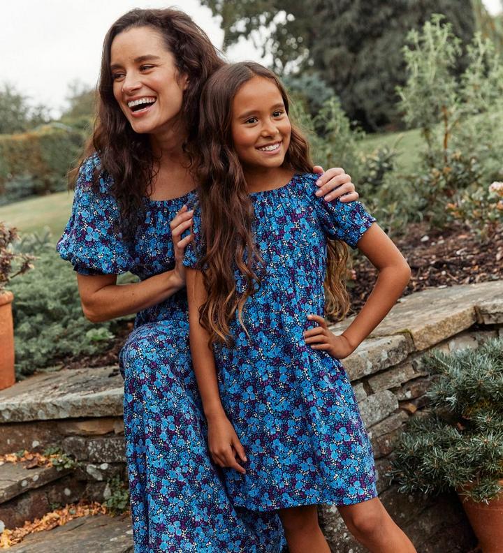 A woman & a girl wearing matching dresses with blue & purple floral print, round neck & short puff sleeves.