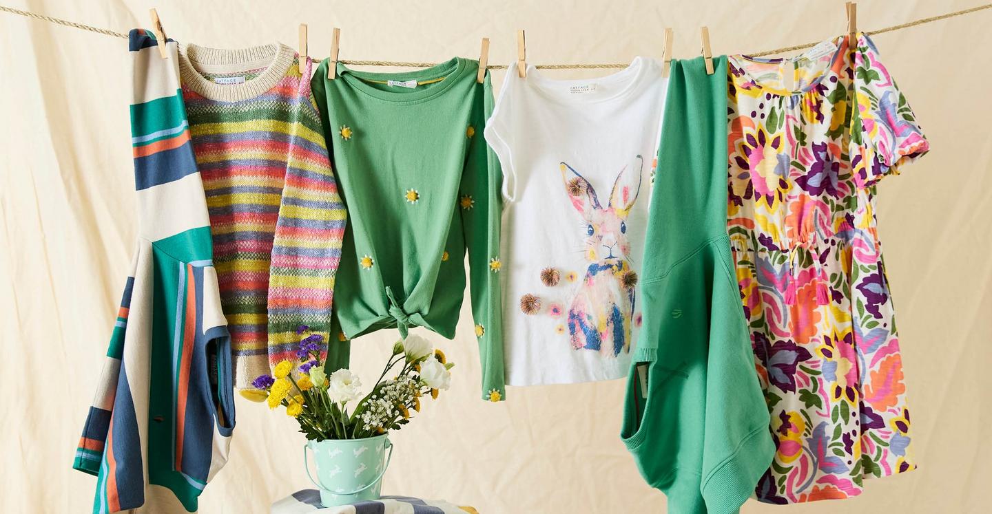A selection of bright, colourful clothes with bold stripes & floral prints, hanging from a clothes line.