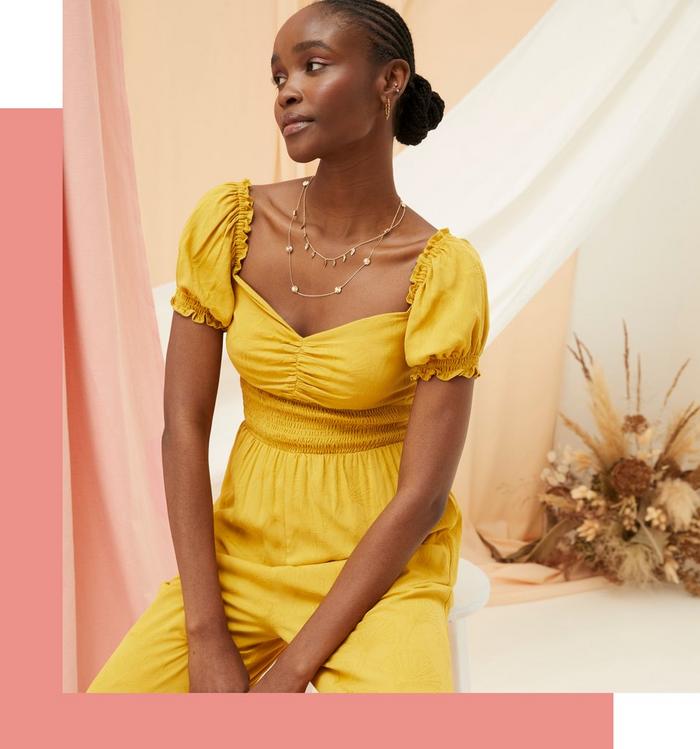 A woman wearing a sunshine-yellow jumpsuit with cap sleeves, sweetheart neckline & shirred waist.