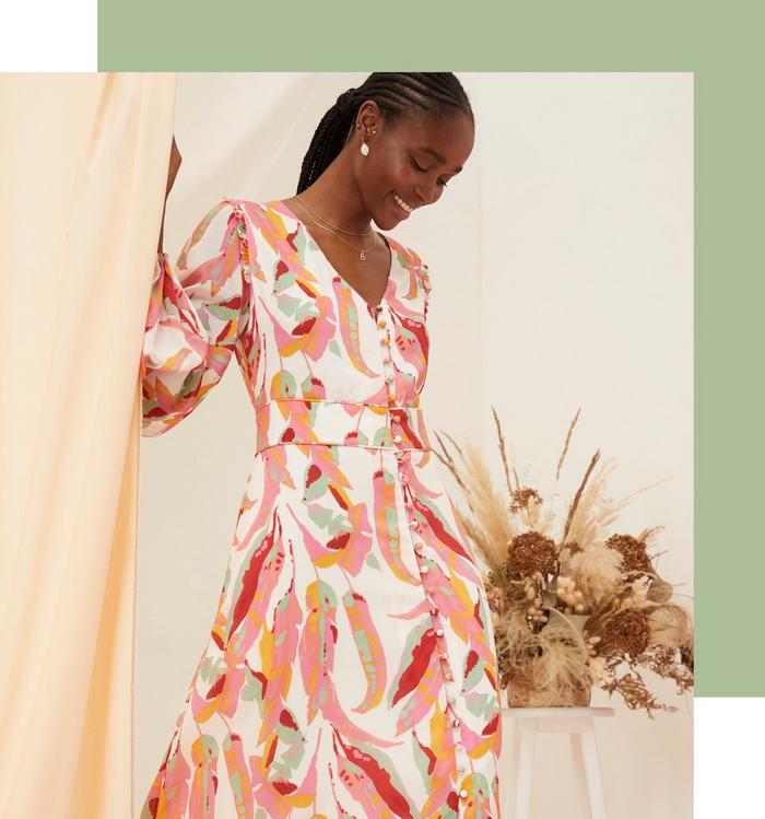 A woman wearing a long-sleeved white maxi dress with bright colourful painted leaves print, V-neck & button-front.