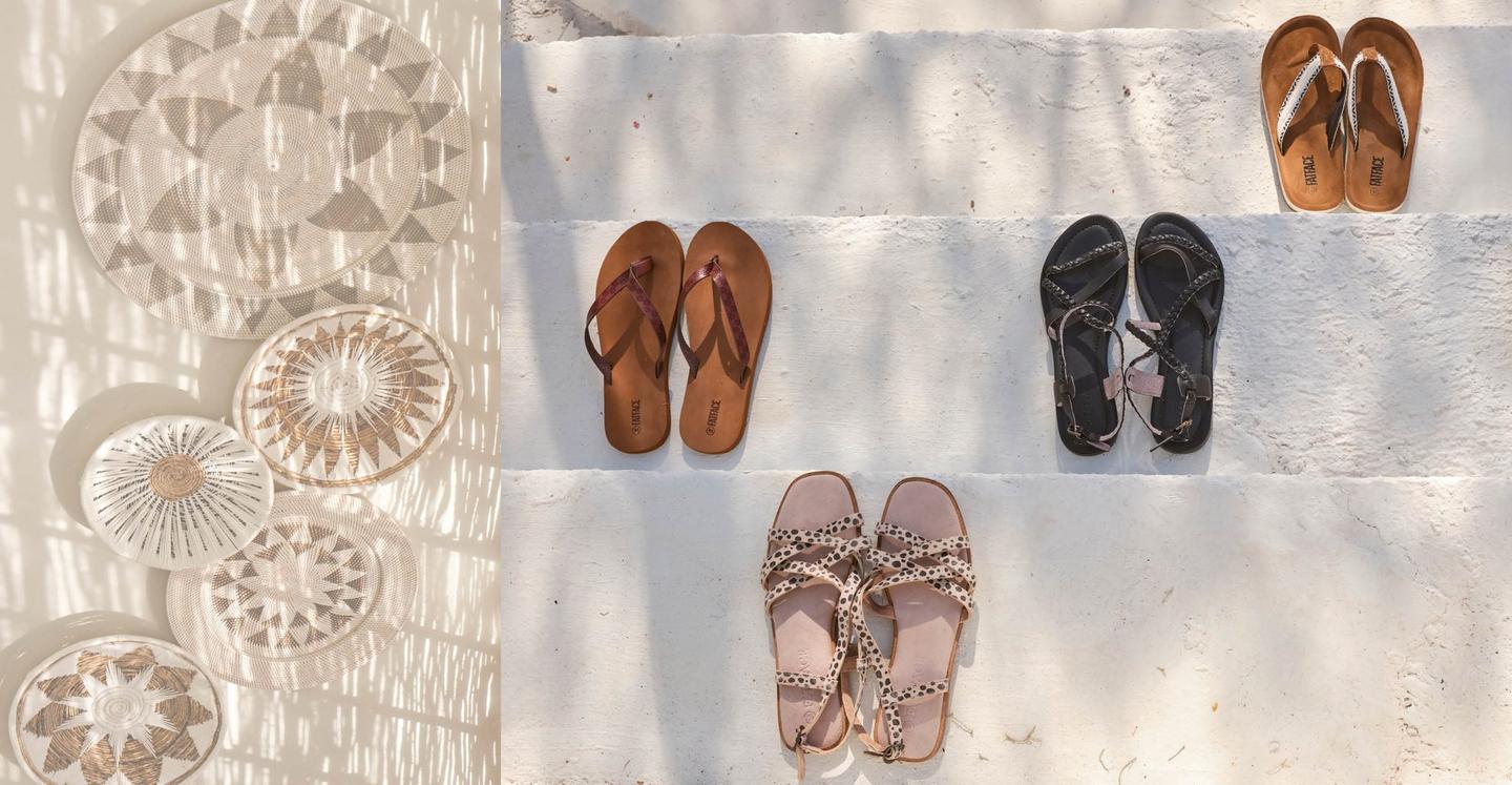 A selection of women's sandals & flip flops laid out in pairs on painted white steps.