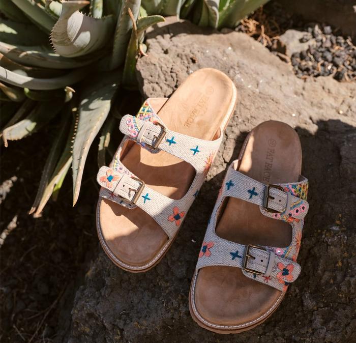 A pair of ivory canvas slide-on sandals, with colorful embroidered patterns & two chunky buckle straps.