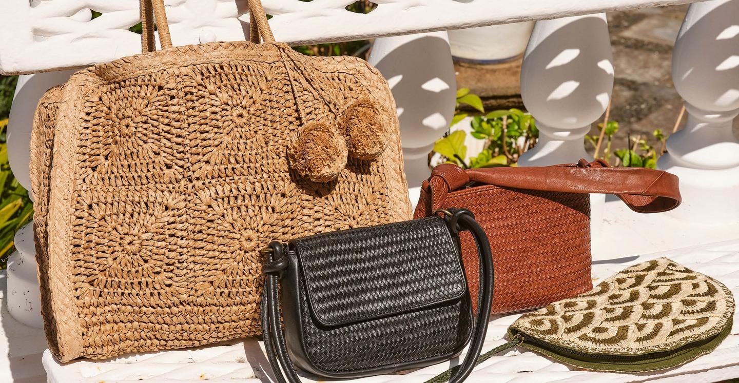 A selection of women's bags, including a large woven straw tote, black & tan brown leather handbags, & a patterned clutch.