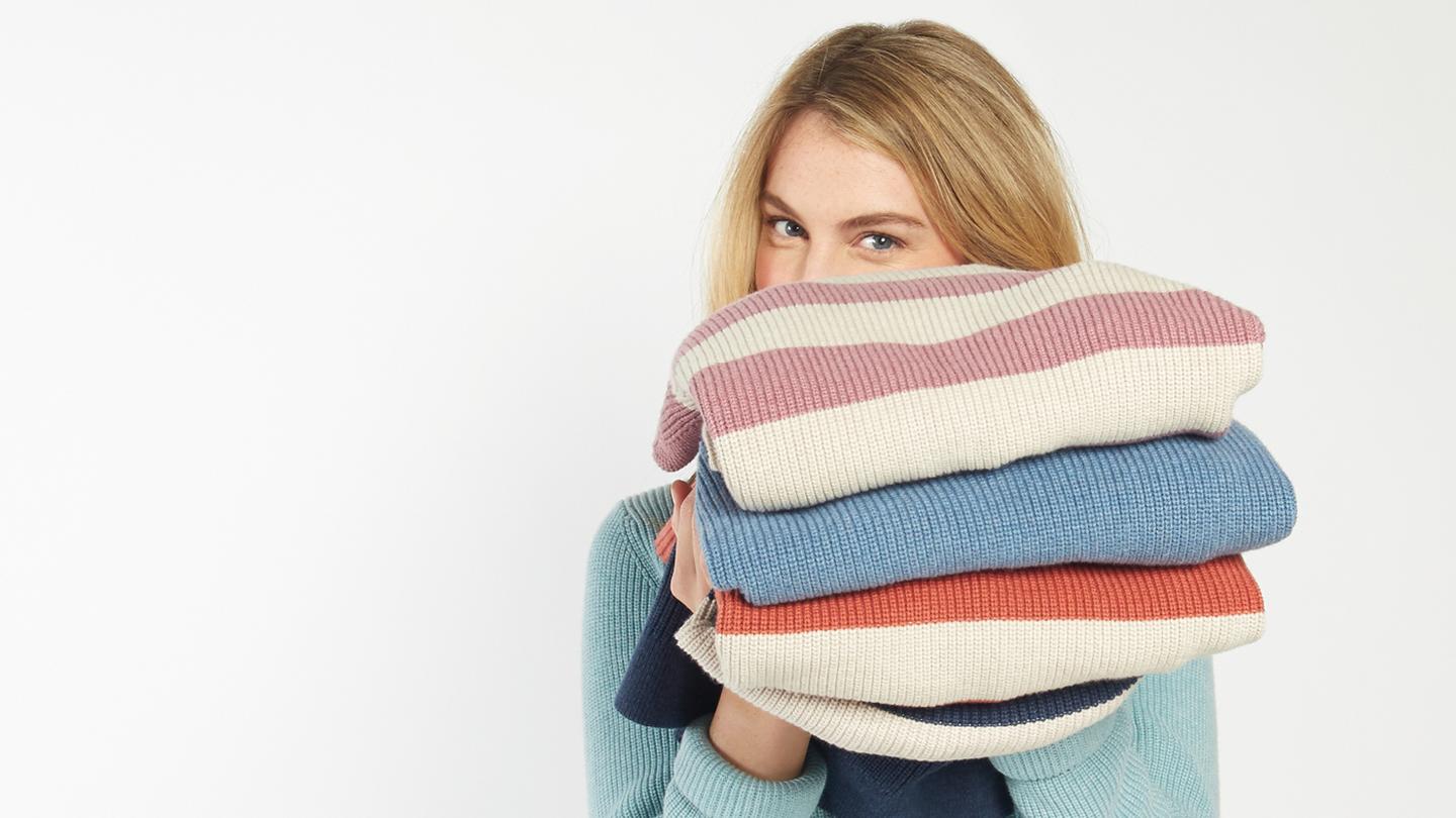 A model holding a stack of our Cally Jumper in loads of colours