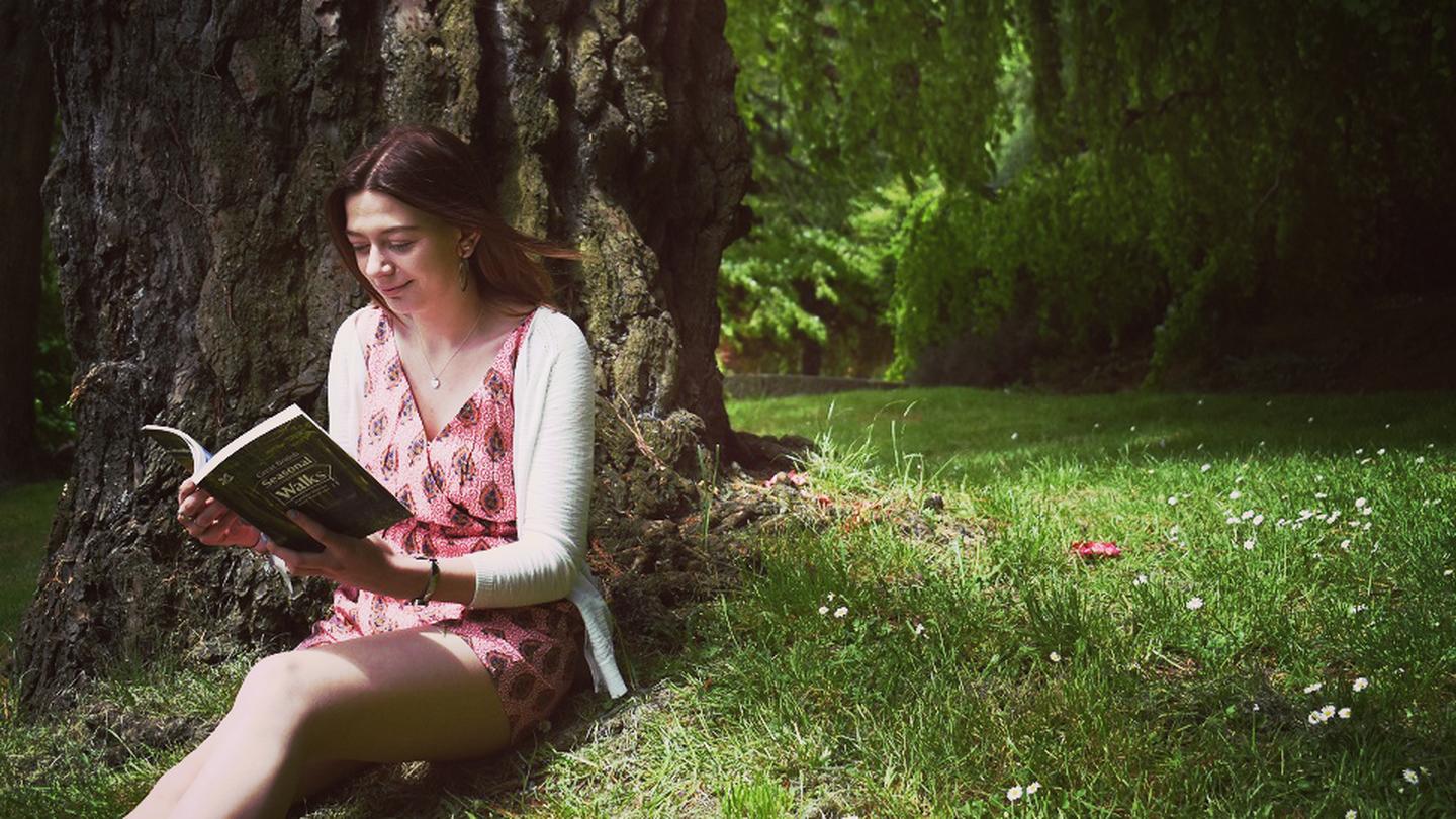 Vicky, store manage of the Truro FatFace store, reading a book in a beautiful park wearing FatFace clothes