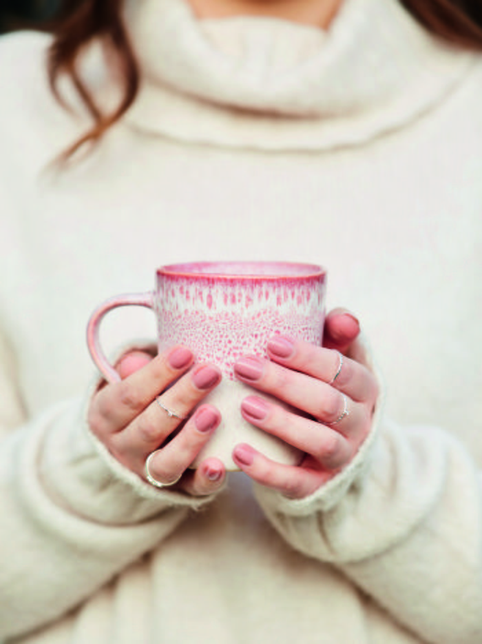 A woman in a cream roll neck jumper holding a Poppy patterned mug in her hands.