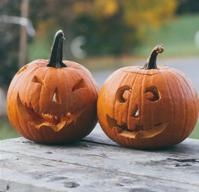 A pair of carved pumpkins sitting on a wooden table.