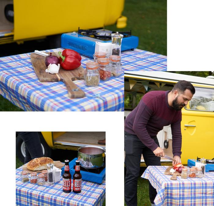Dark haired male wearing a red jumper cutting up vegetables on a camping table outdoors