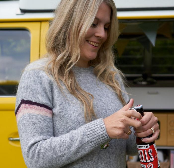 Blonde haired girl wearing a grey jumper opening a bottle of beer