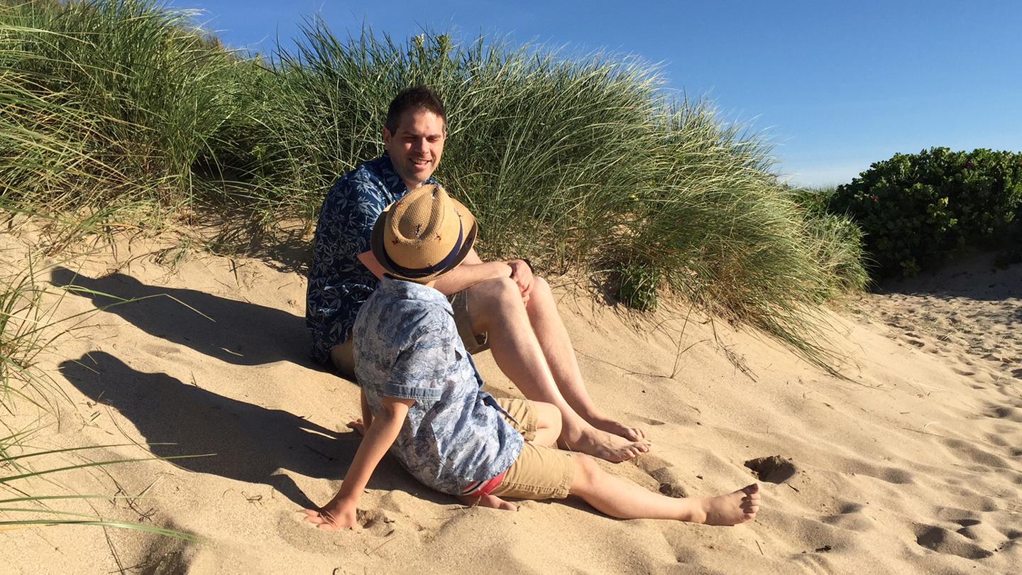Stu, store manager at FatFace Fistral, on the beach at Fistral with his son, in FatFace clothes