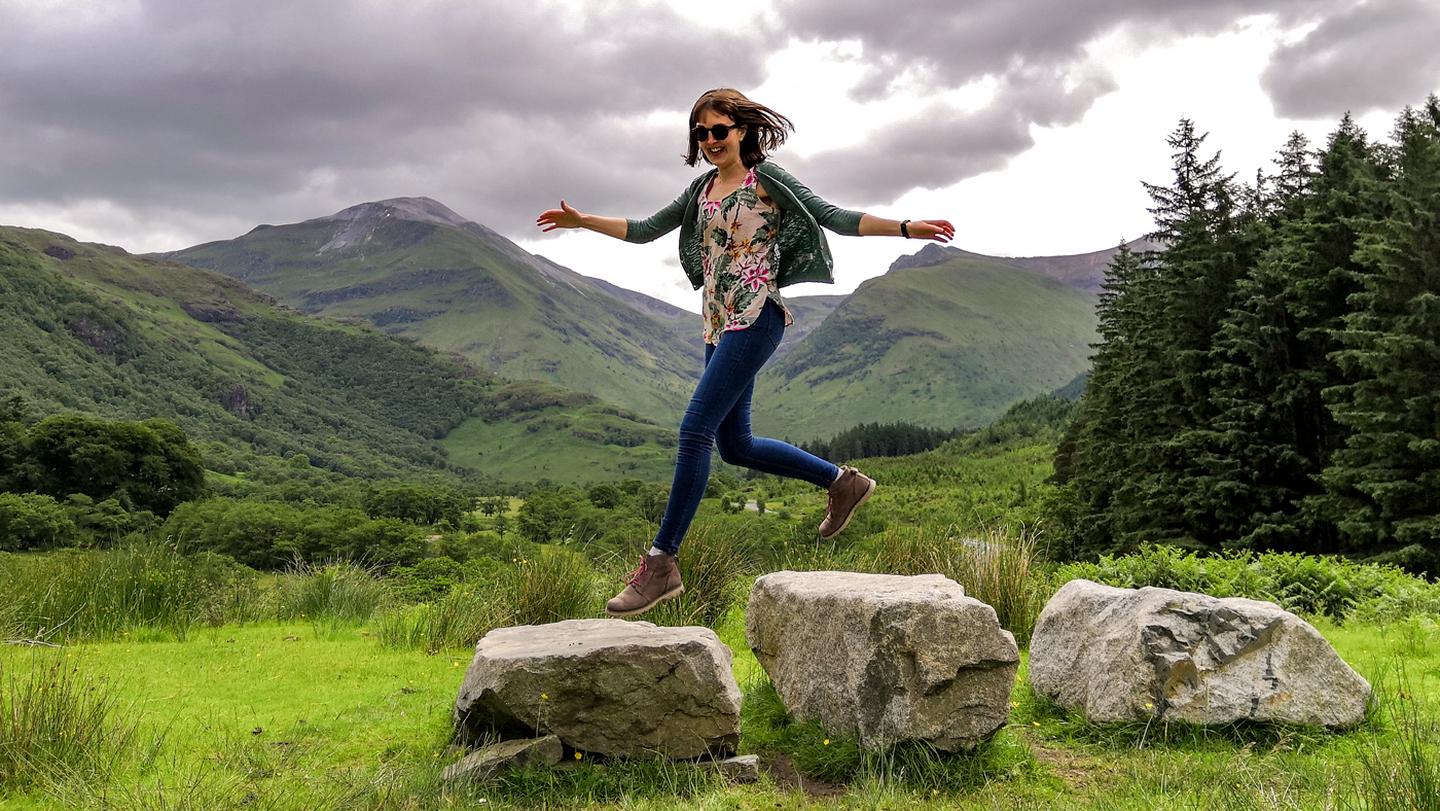 Rachel, store manager at FatFace, jumps along some rocks on Ben Nevis, wearing FatFace clothes