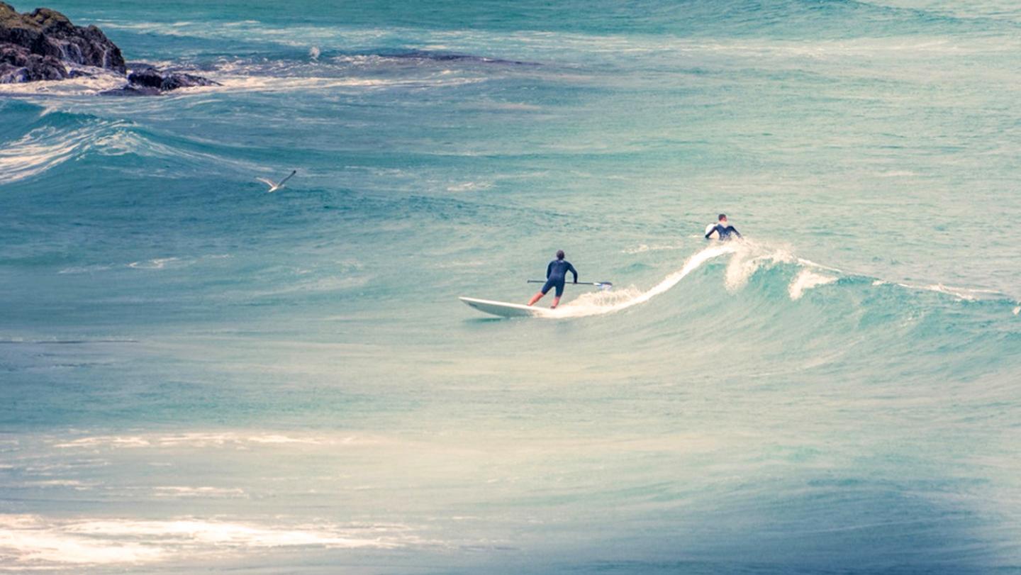 A couple of paddleboarders hitting the waves in Fistral, Cornwall