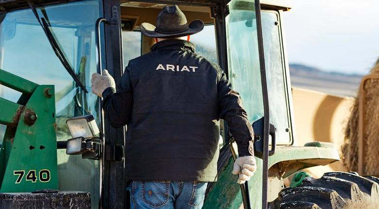 man wearing Ariat softshell jacket getting into a tractor
