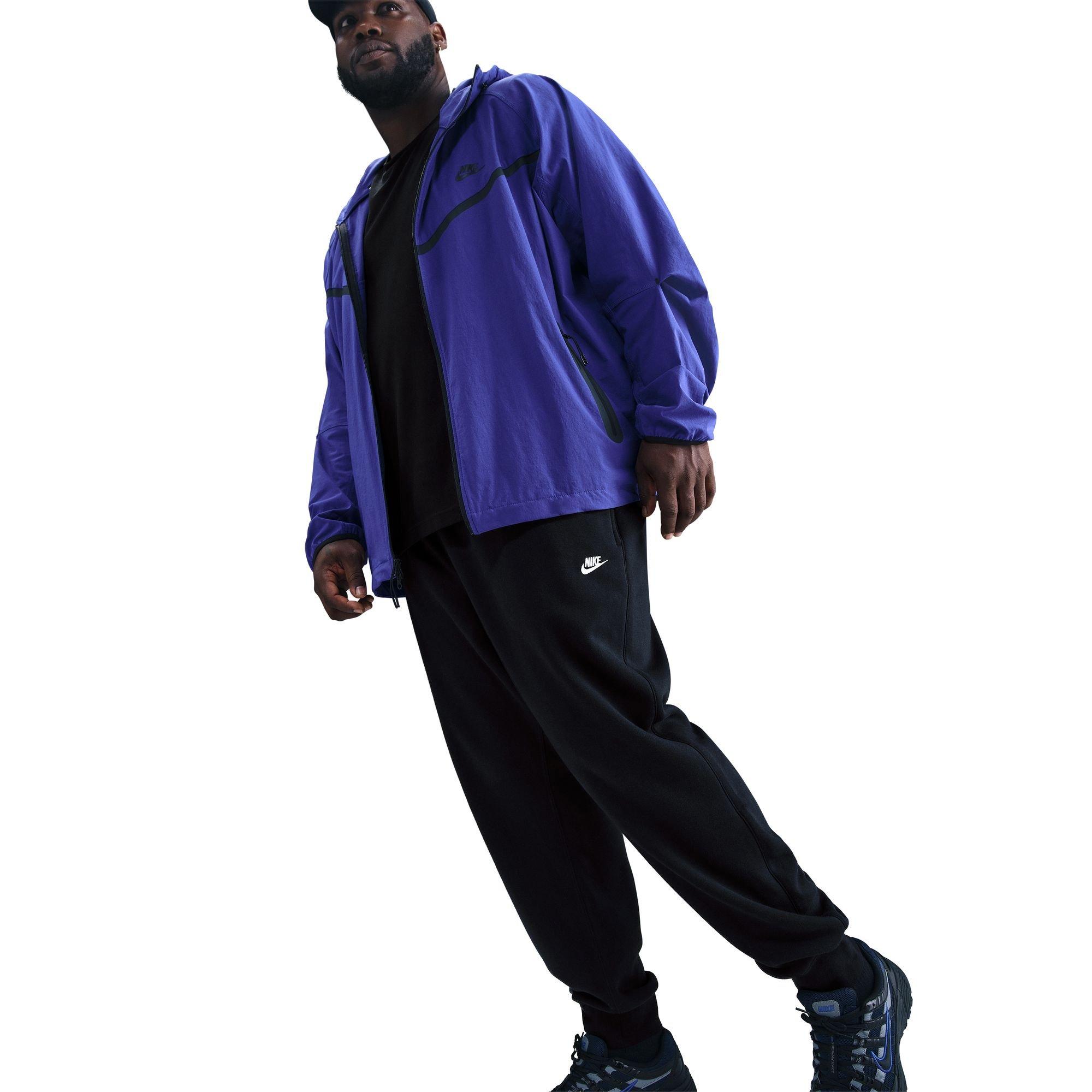 Side view of man wearing black Nike Club Joggers with purple jacket demonstrating casual layering style