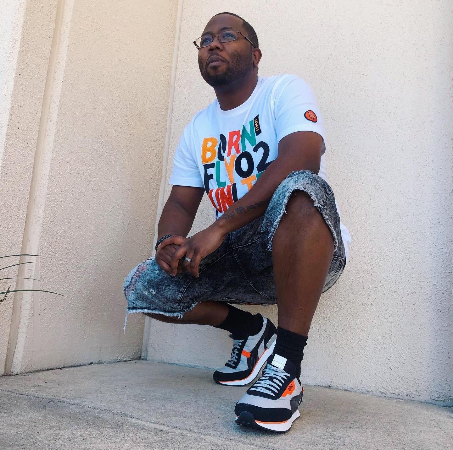 Man in Born Fly white tee, denim shorts and a pair of Puma Future Rider sneakers.
